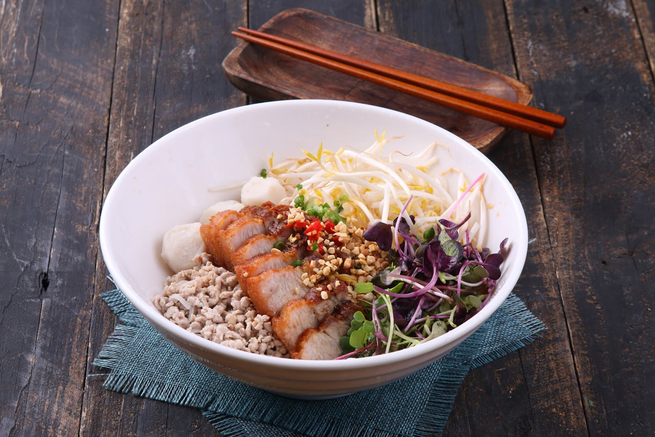A flavorful Asian noodle bowl with crispy pork, fresh vegetables, and peanuts. Perfect for food enthusiasts.