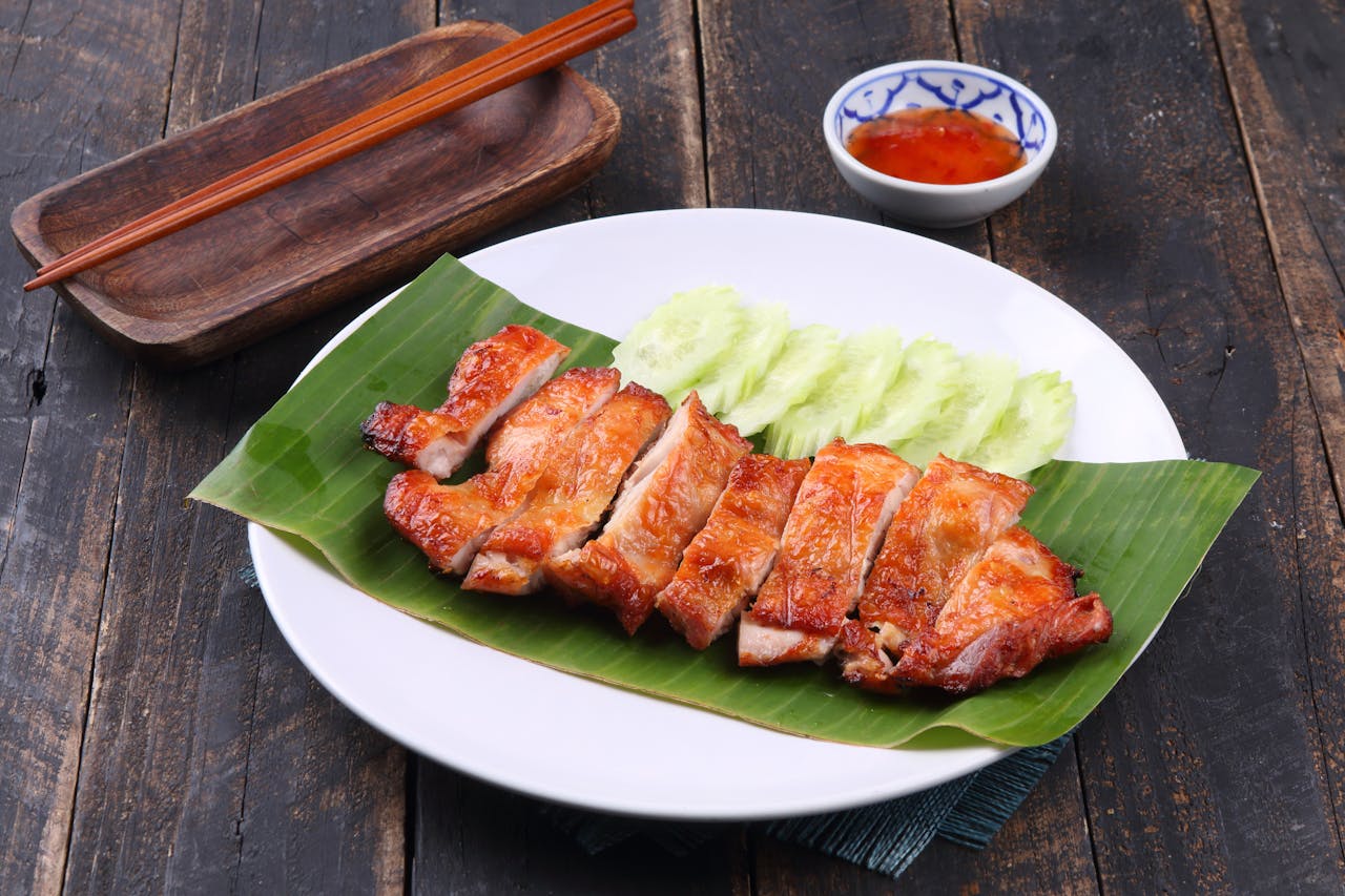 Delicious grilled chicken served with cucumber slices and sauce on a banana leaf.
