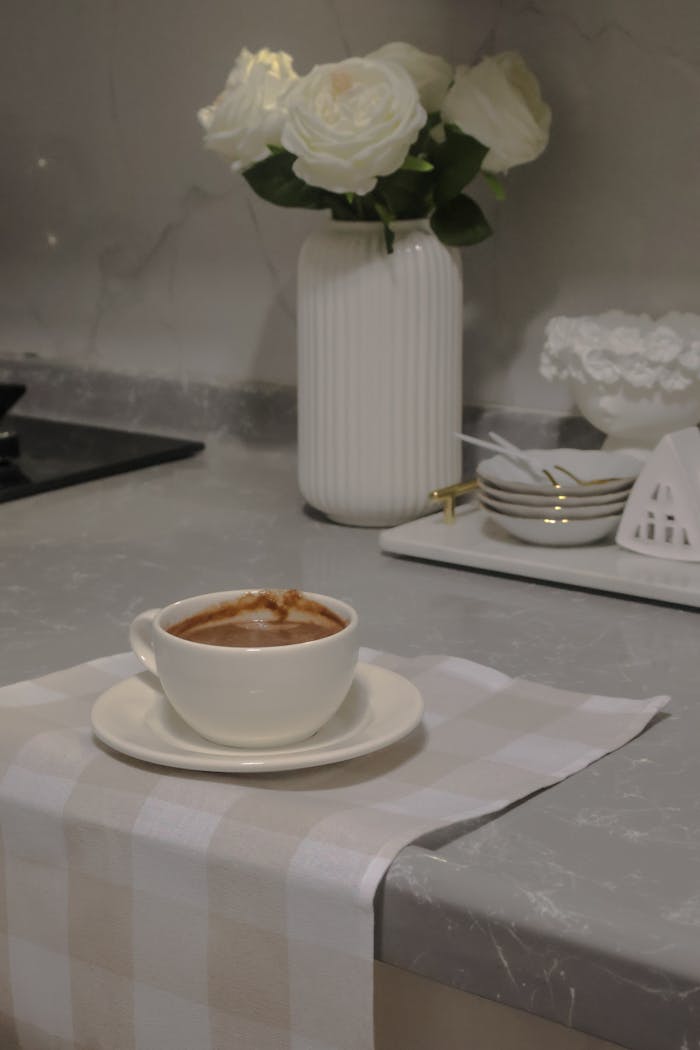 Cup of coffee on a marble counter with elegant decor and white flowers.